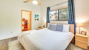 Una camera da letto con un letto grande, una ventola a soffitto, una finestra con tende, un comodino con una lampada e un tavolino da notte con una cornice.