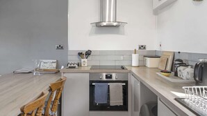 Uma cozinha moderna com forno embutido, coifa de aço inoxidável e mesa de jantar de madeira com cadeiras.