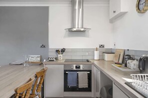 A modern kitchen with a built-in oven, a stainless steel range hood, and a wooden dining table with chairs. - Beach House & Garden in St Merryn, Private Parking (Rock)