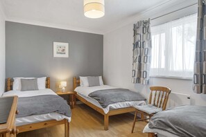 A hotel room with two single beds, a wooden chair, a small table, and a window with patterned curtains. - Beach House & Garden in St Merryn, Private Parking (Rock)