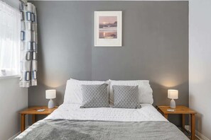 A bedroom with a grey wall, a framed picture, two patterned pillows, a white bedspread, and two bedside lamps. - Beach House & Garden in St Merryn, Private Parking (Rock)