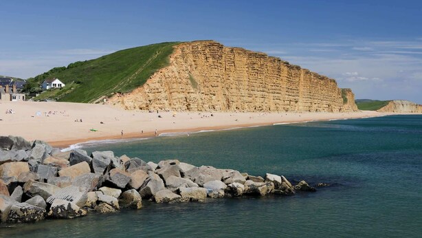 A coastal beach with a prominent cliff, a sandy shore, and a rocky breakwater. - 18th Century Thatched Cottage, Parking & Garden (Dorset)