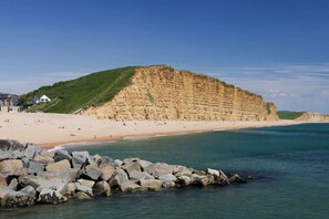 A coastal beach with a prominent cliff, a sandy shore, and a rocky breakwater.