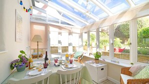 A conservatory with a table set for tea, surrounded by wicker furniture and potted plants. - 18th Century Thatched Cottage, Parking & Garden (Dorset)