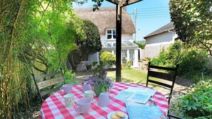 A round table with a checkered tablecloth, surrounded by chairs, with a newspaper, a plate with cookies, and a vase with flowers. - 18th Century Thatched Cottage, Parking & Garden (Dorset)