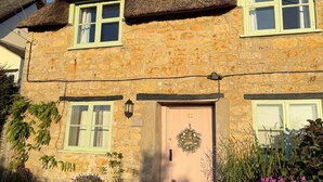 A stone house with a thatched roof, a pink door, and a visible front garden with potted plants and flowers. - 18th Century Thatched Cottage, Parking & Garden (Dorset)