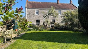 Une maison en pierre avec un toit en pente, un petit jardin devant et un banc.