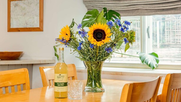 A dining table with a bottle of apple juice, a glass, and a vase of flowers. - Grade II Listed House, Tranquil Garden & Parking (Kingsdon)