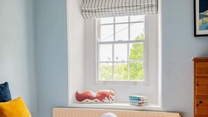 A bedroom with a bed, a window with a view of greenery, a radiator, a wooden dresser, and a stuffed toy on the windowsill. - Grade II Listed House, Tranquil Garden & Parking (Kingsdon)