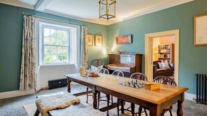 Une pièce chaleureuse avec une table en bois, des chaises, un radiateur, une bibliothèque et une fenêtre avec des rideaux.
