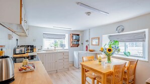 A modern kitchen with white cabinets, a wooden dining table, and a view of the outside through large windows. - Grade II Listed House, Tranquil Garden & Parking (Kingsdon)
