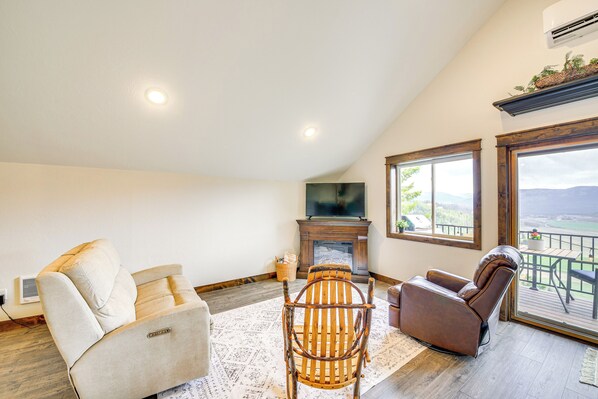 A living room with a fireplace, a television, and a view of the outdoors. - Balcony & Patio w/ Mtn Views! Bonners Ferry Escape (Bonners Ferry)