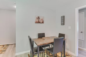Een eetgedeelte met een vierkante tafel, vier stoelen, een tapijt met een patroon en twee decoraties aan de muur.