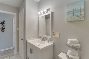 Een badkamer met een witte wastafel, een spiegel met verlichting, een toilet en een handdoekhouder.