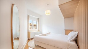 Une chambre à coucher avec un grand lit, une table de chevet, un miroir, une fenêtre avec des rideaux et un luminaire suspendu.