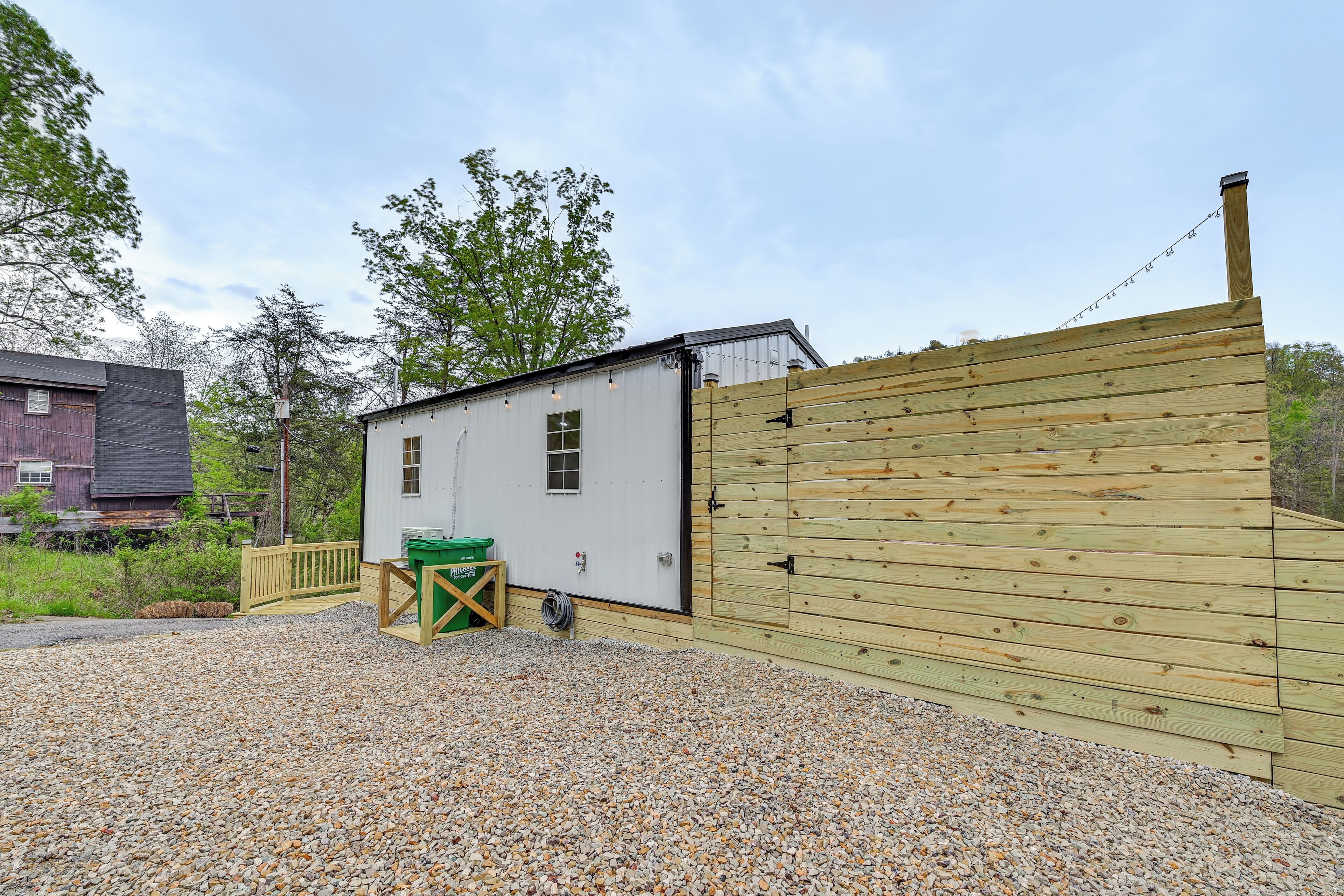 A gravel driveway leading to a white building with a wooden fence and a wooden gate.