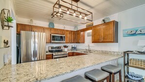 A kitchen with granite countertops, stainless steel appliances, wooden cabinets, and bar stools. - Balcony w/ Pool & Beach Views: Gulf Shores Condo! (Gulf Shores)
