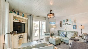 A living room with a television, sofa, ottoman, and a ceiling fan. - Balcony w/ Pool & Beach Views: Gulf Shores Condo! (Gulf Shores)