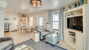 A spacious living room with a dining area, a sofa, a television, and a chandelier. - Balcony w/ Pool & Beach Views: Gulf Shores Condo! (Gulf Shores)