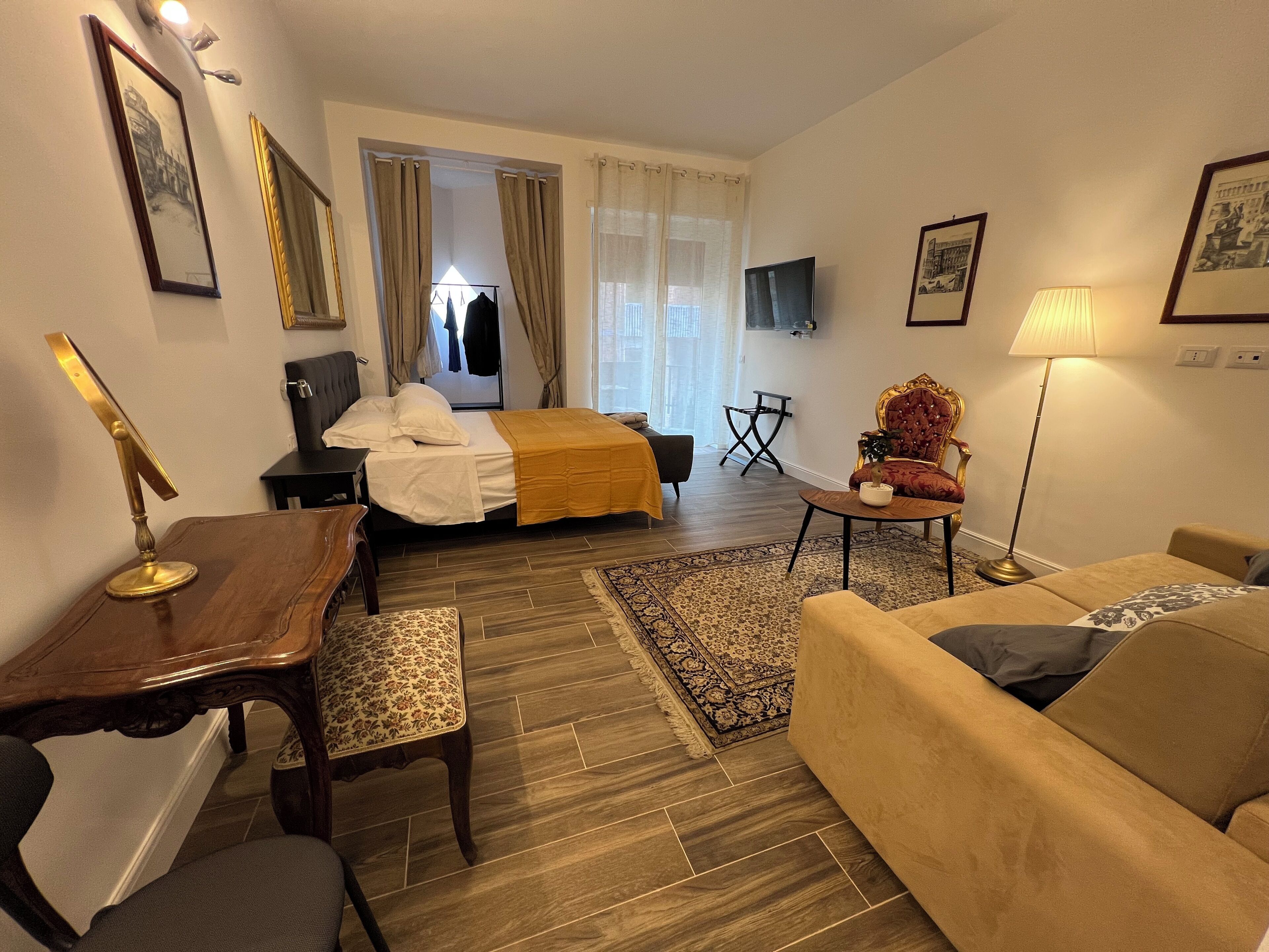 A hotel room with a bed, a desk, a chair, a sofa, a TV, and a lamp.