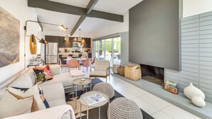 A modern living room with a fireplace, seating area, and kitchen in the background.