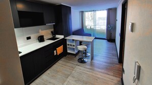 Una cocina moderna con armarios negros, una encimera blanca y un horno empotrado. Hay una zona de comedor con una mesa y sillas, y un ventanal con cortinas.