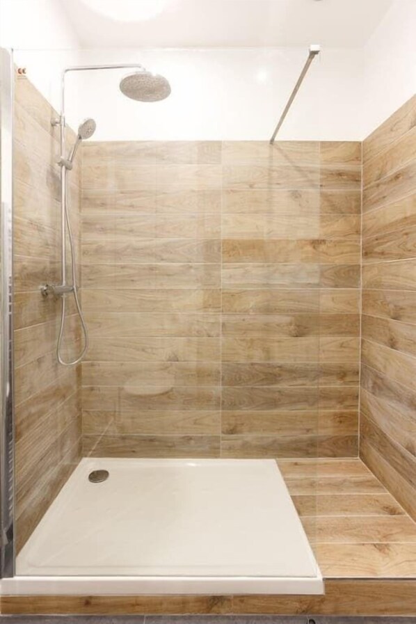 Une douche à l’italienne avec une porte en verre, des murs carrelés et un sol de douche blanc.