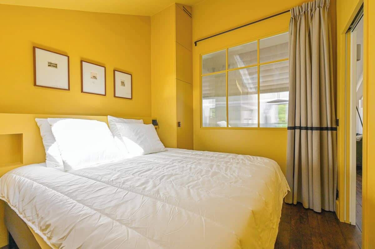 A room with a large bed, yellow walls, and a window with curtains.