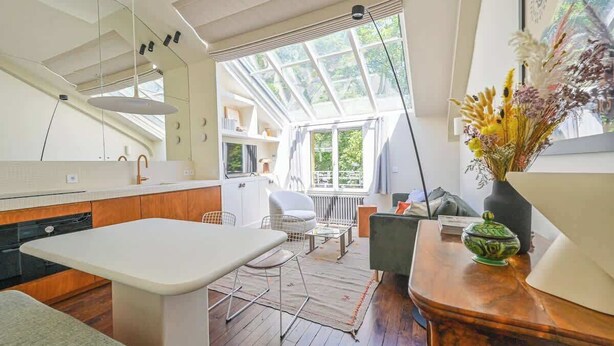 A modern kitchen with a large island, a dining area with a table and chairs, and a view through a skylight to an outdoor area. - Sublime loft - Montmartre (Paris)