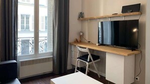 Una habitación moderna con un escritorio de madera, televisión, una silla y una ventana con cortinas.