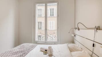 A hotel room with a bed, a window with a view of buildings, and a bedside table with a lamp.