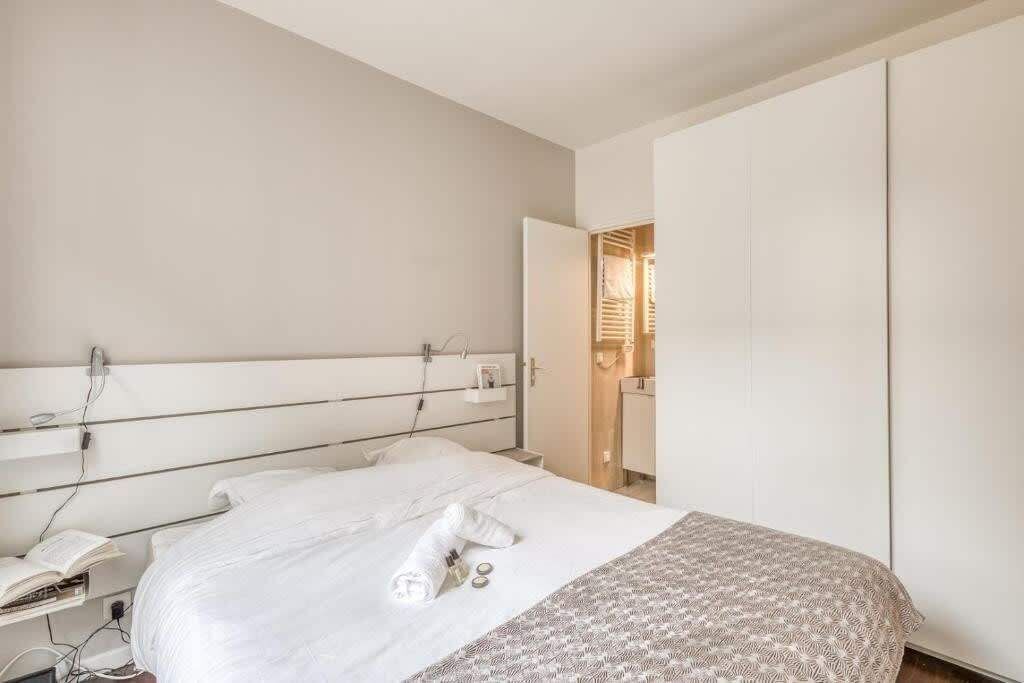 A modern hotel room with a large bed, a bedside table with a lamp, and a wardrobe.