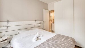 Una habitación de hotel moderna con una cama grande, una mesita de noche con lámpara y un armario.