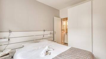 A modern hotel room with a large bed, a bedside table with a lamp, and a wardrobe.