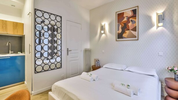 Ein Hotelzimmer mit einem Bett, einem an der Wand befestigten Spiegel, einem Gemälde und einem kleinen Tisch mit Blumen.