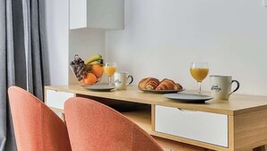 Ein moderner Essbereich mit einem Holztisch, zwei Stühlen, einer Obstschale, Croissants und zwei Gläser Orangensaft.