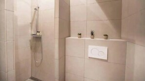 Ein modernes Badezimmer mit Dusche, einer an der Wand montierten Bedienkonsole und drei kleinen Topfpflanzen auf einem Regal.