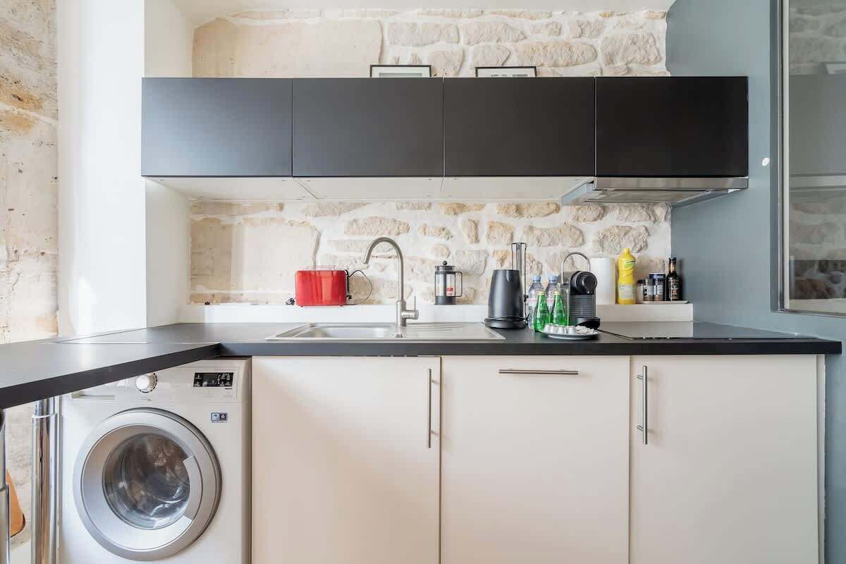 A compact kitchen with a washing machine, a sink, and a stone wall backsplash.