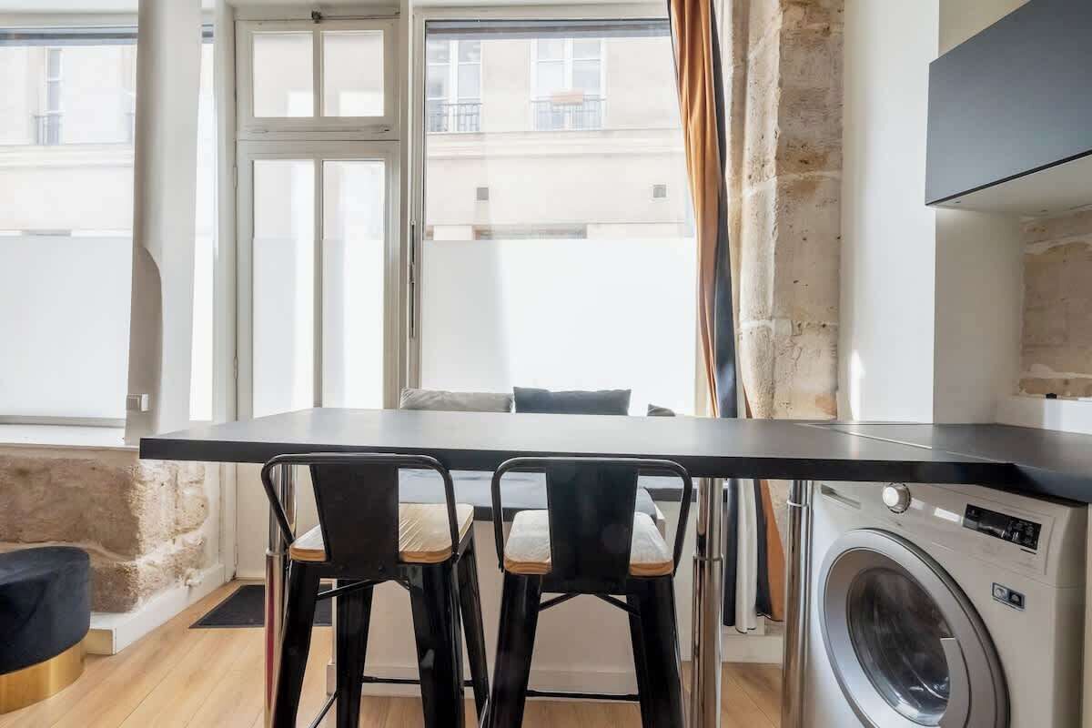 A compact kitchen with a dining area, a washing machine, and a large window with curtains.
