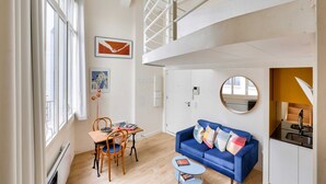 Een modern appartement met een eetgedeelte, een blauwe bank, een keuken en een vide.