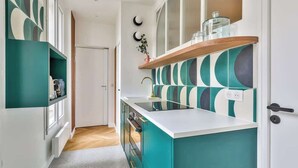 A modern kitchen with teal cabinetry, a white countertop, and a wooden shelf above the sink.