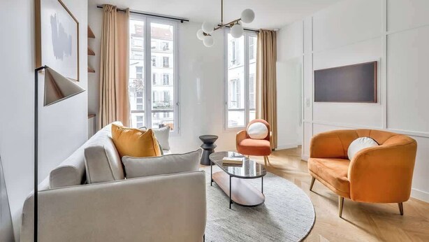 A modern living room with a sofa, armchairs, a coffee table, and a TV on the wall.