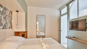 A modern hotel room with a large bed, a mirror, a TV, and a wooden shelf.