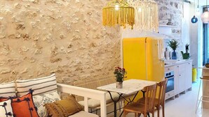Una sala de estar moderna con una pared de piedra, un sofá con cojines, una mesa de comedor con sillas y un mueble de color amarillo.