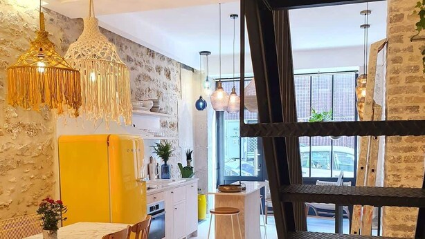 Una cocina moderna con armarios blancos, un comedor amarillo y lámparas colgantes.
