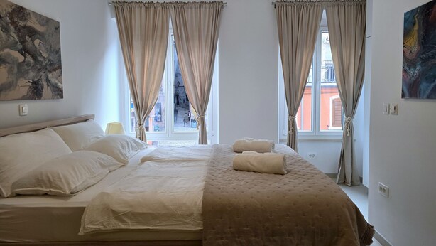Ein Schlafzimmer mit einem Bett, beigefarbenen Vorhängen und einem Bild an der Wand.