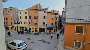 Straßenansicht mit Gebäuden, einem weißen Auto und einem schwarzen Auto, das am Straßenrand geparkt ist.