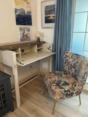 Une pièce avec un bureau en bois, un fauteuil à motifs floraux et des œuvres d’art accrochées au mur.