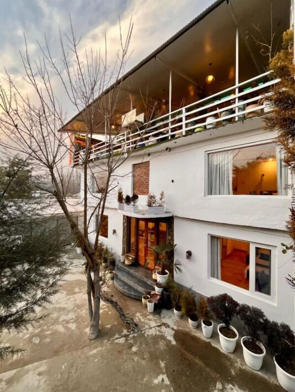 A two-story building with a balcony, potted plants, and a visible interior from the windows. - Dojee's Cottages (Srinagar)