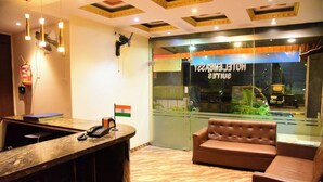 A reception area with a marble counter, a telephone, a small Indian flag, and a leather sofa. - Hotel Embassy Suites (Mumbai)